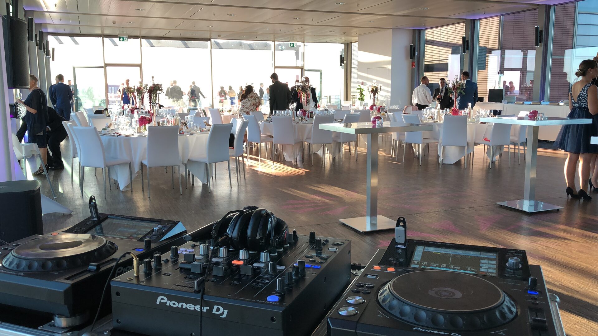 DJ-Pult im Vordergrund mit Blick auf Empfang und Tanzfläche in einem verglasten Eventraum